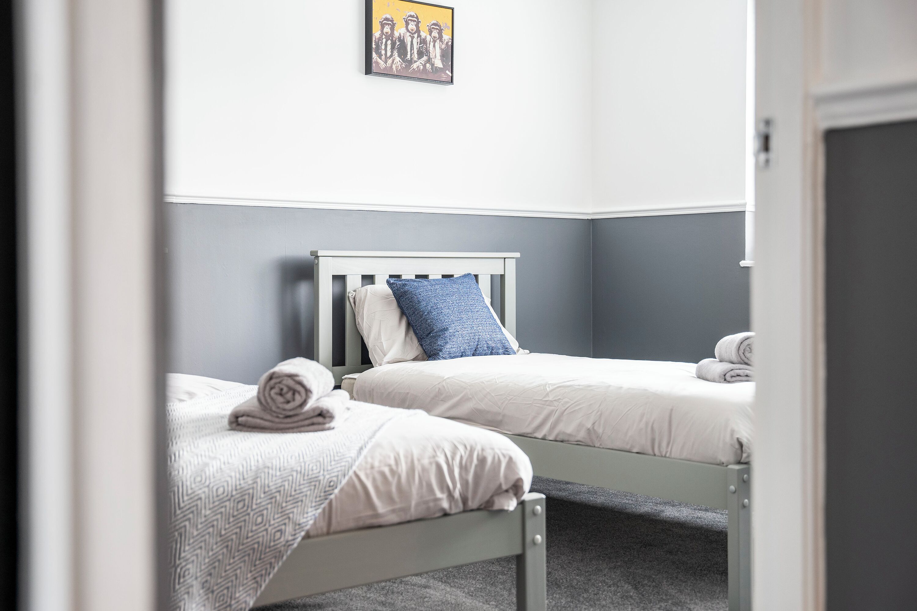 A bedroom with two single beds, a gray wall, and a framed picture above the beds.