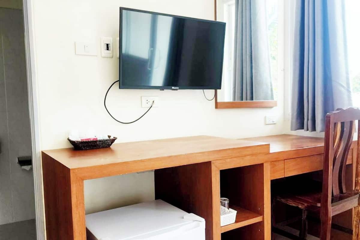 Habitación de hotel con escritorio de madera, televisor, refrigerador pequeño, espejo y ventana con cortinas.