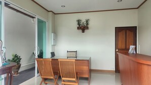 Um quarto com uma escrivaninha de madeira, duas cadeiras, um armário pequeno, uma porta e um balcão de recepção.