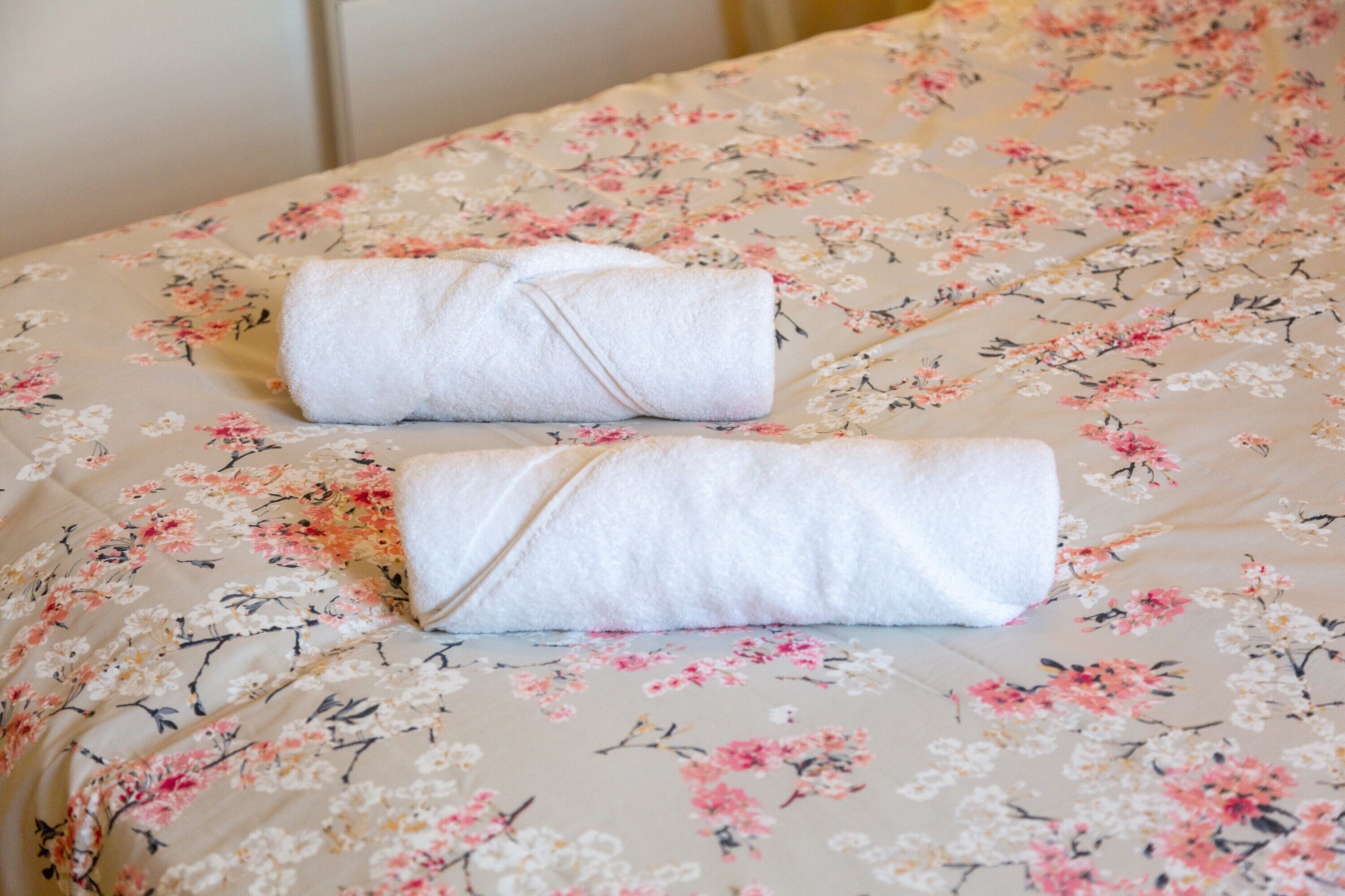 A bed with a floral-patterned bedspread and two neatly folded white towels.