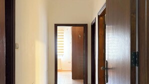 Un couloir avec un sol carrelé, des portes en bois et un luminaire au plafond.