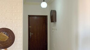 Un couloir avec une porte en bois, un ventilateur fixé au mur et un luminaire suspendu au plafond.