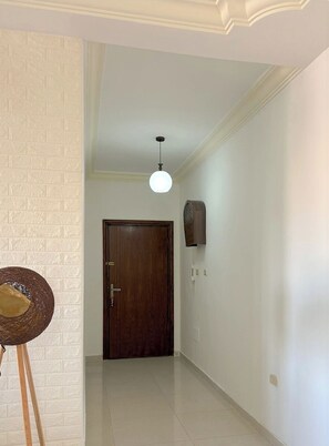 Ein Flur mit einer Holztür, einem Wandventilator und einer Pendelleuchte.