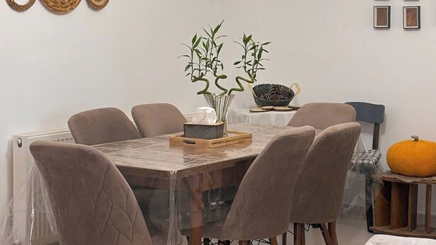 Un coin repas avec une table ronde, six chaises, un vase avec des plantes et une citrouille posée sur une petite table d’appoint.