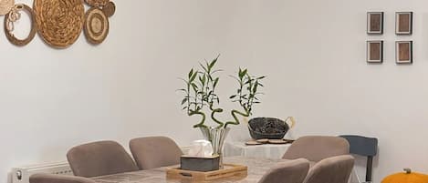 A dining area with a round table, six chairs, a vase with plants, and a pumpkin on a side table.