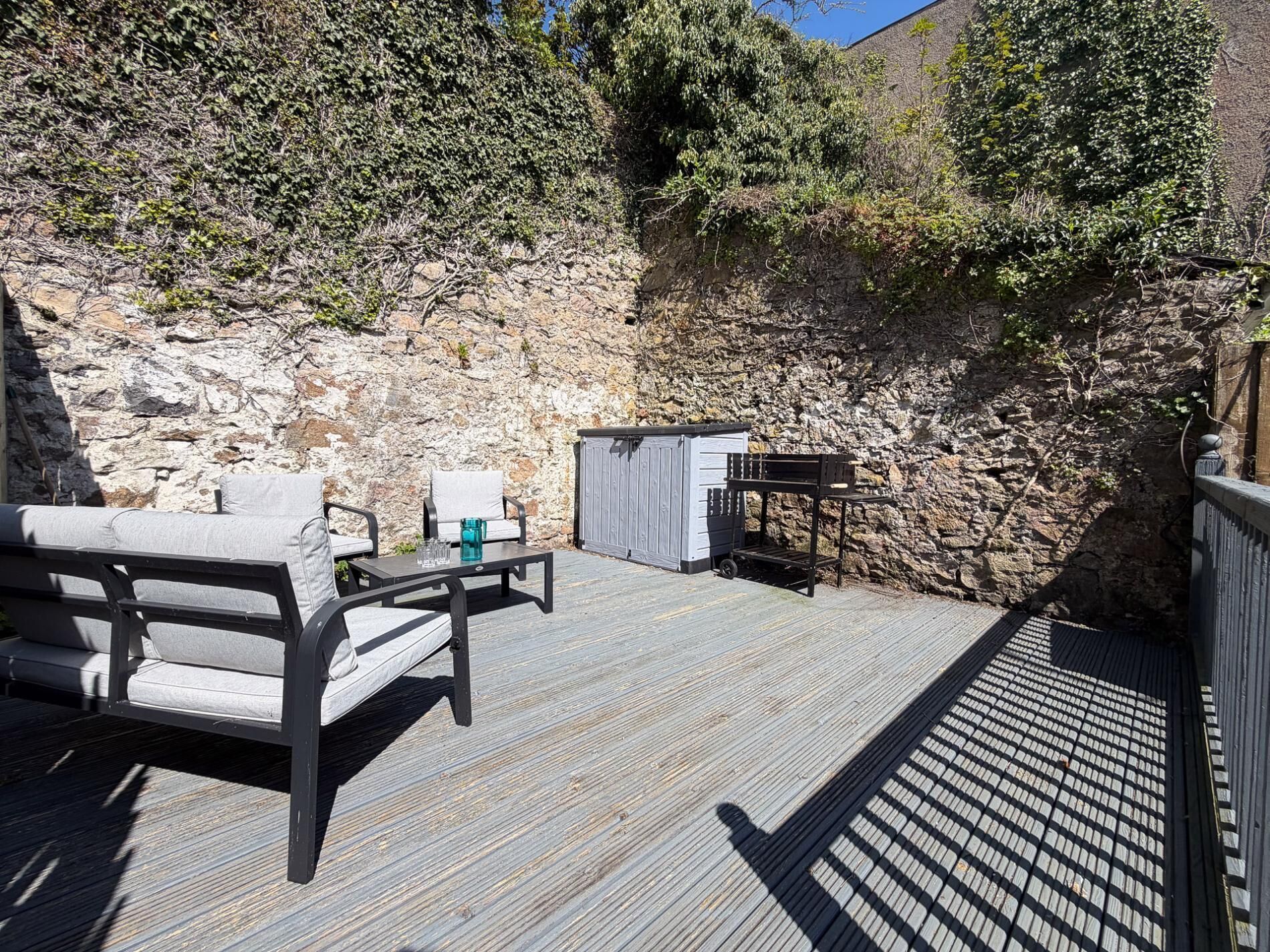 A wooden deck with outdoor furniture, a small shed, and a stone wall.