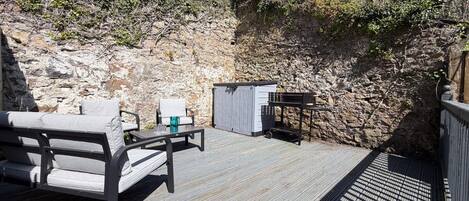 A wooden deck with outdoor furniture, a small shed, and a stone wall.