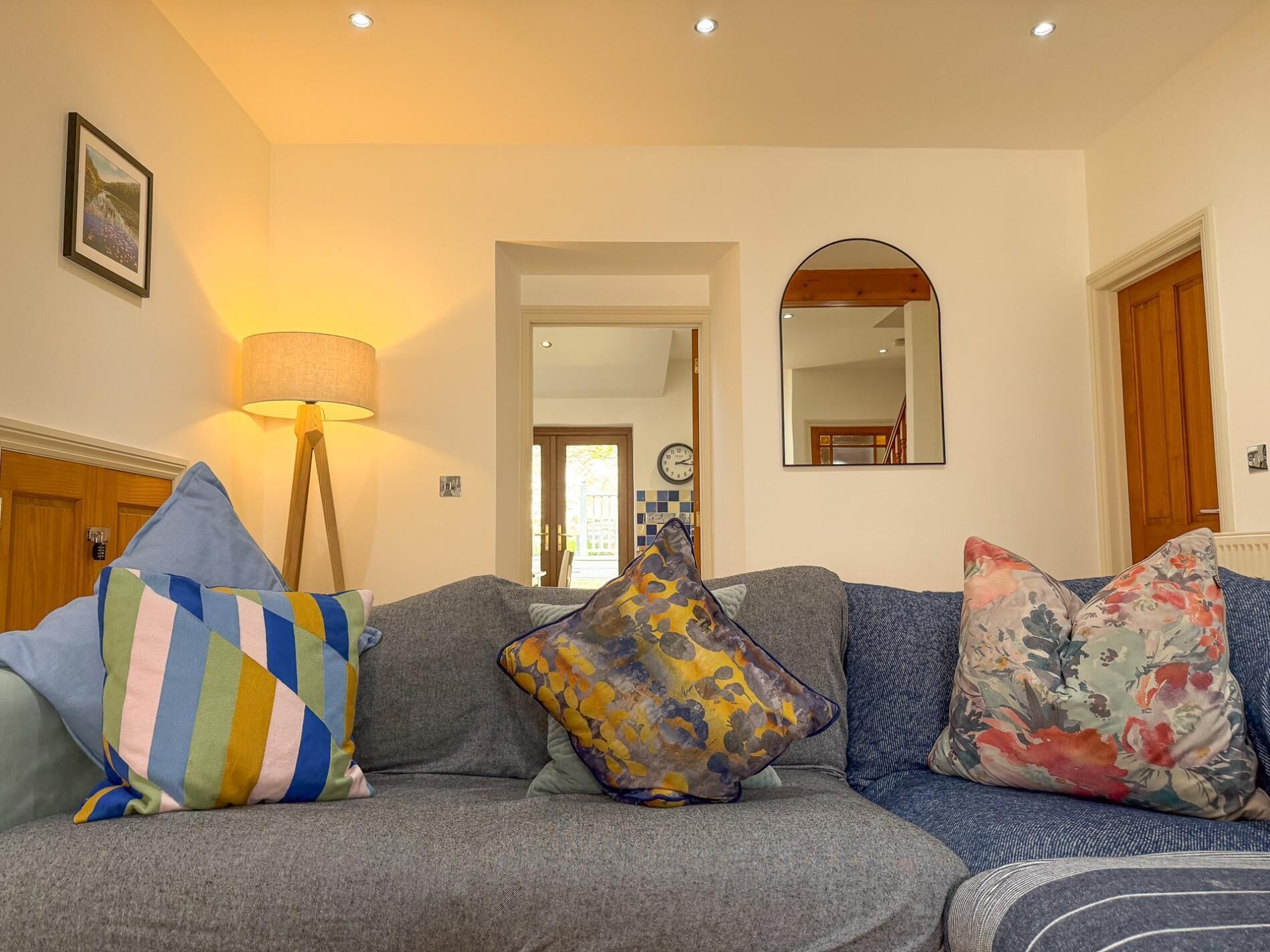 A living room with a sofa, a lamp, a mirror, and a door.