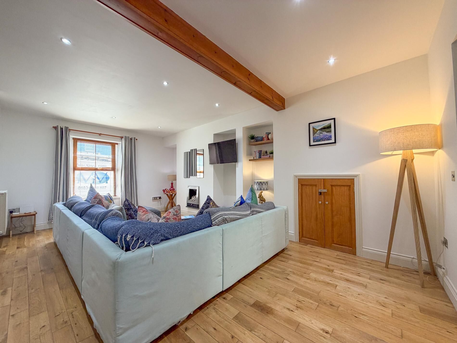 A spacious living room with a large sofa, wooden flooring, a television, and a wooden door.