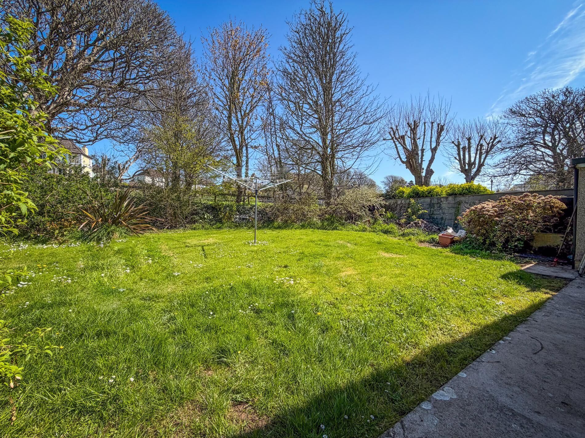 A well-maintained grassy yard with a metal structure, surrounded by trees and a stone wall.