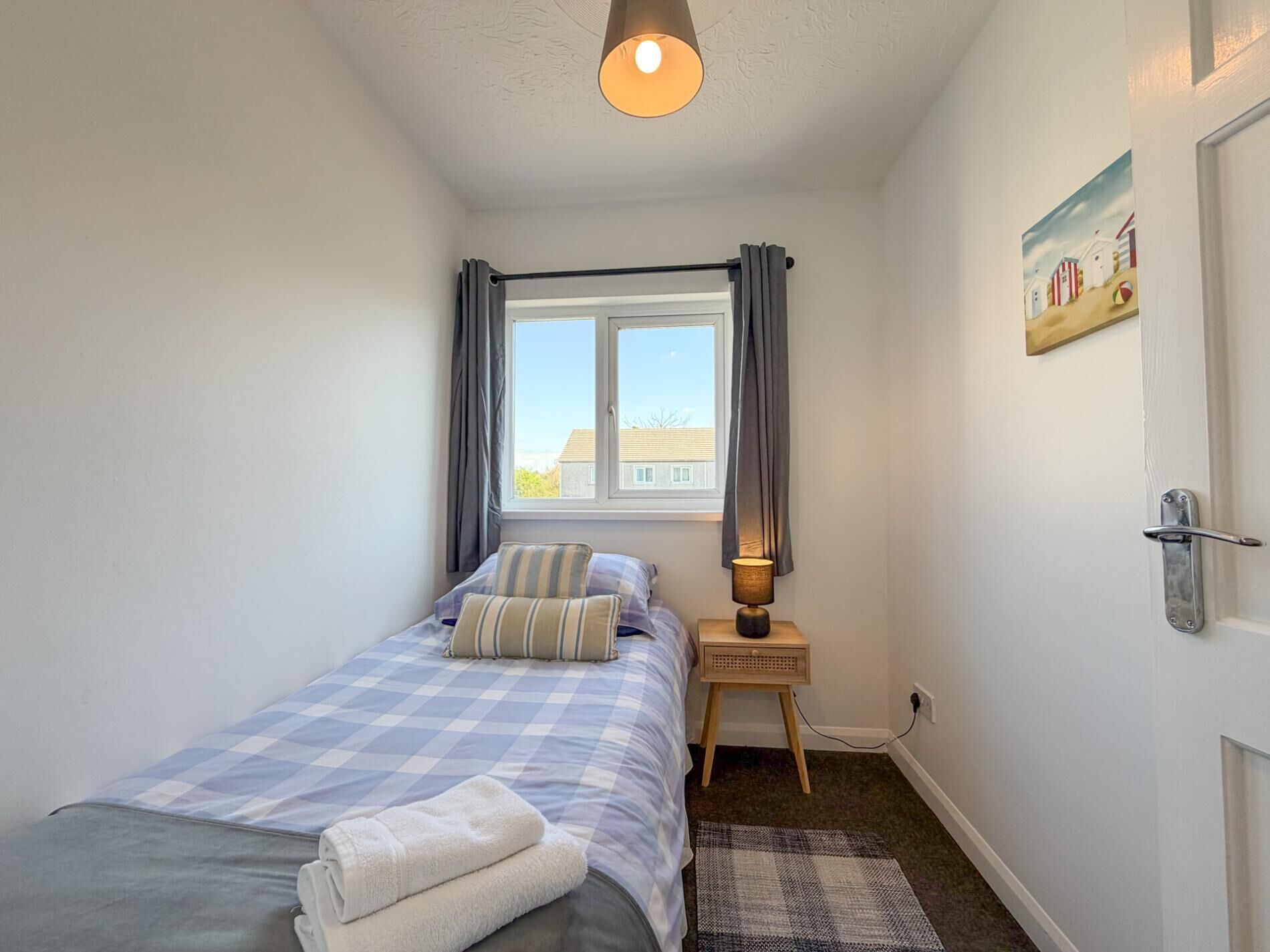 Un dormitorio con cama, ventana, lámpara, cuadro y puerta.