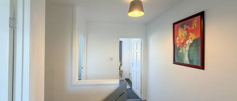 A hallway with a staircase, a light fixture, and a framed painting on the wall.