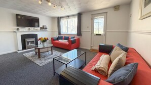 A living room with a fireplace, a red sofa, a glass coffee table, and a TV mounted on the wall. - Pleasant View - 3 Bedroom Holiday Home - Pembroke (Pembroke)
