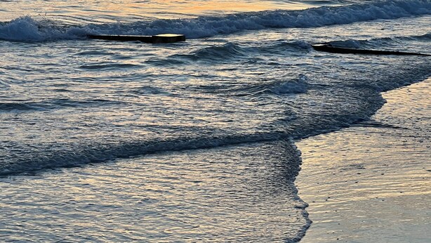 Um pôr do sol sobre o oceano, com ondas avançando em direção à praia.