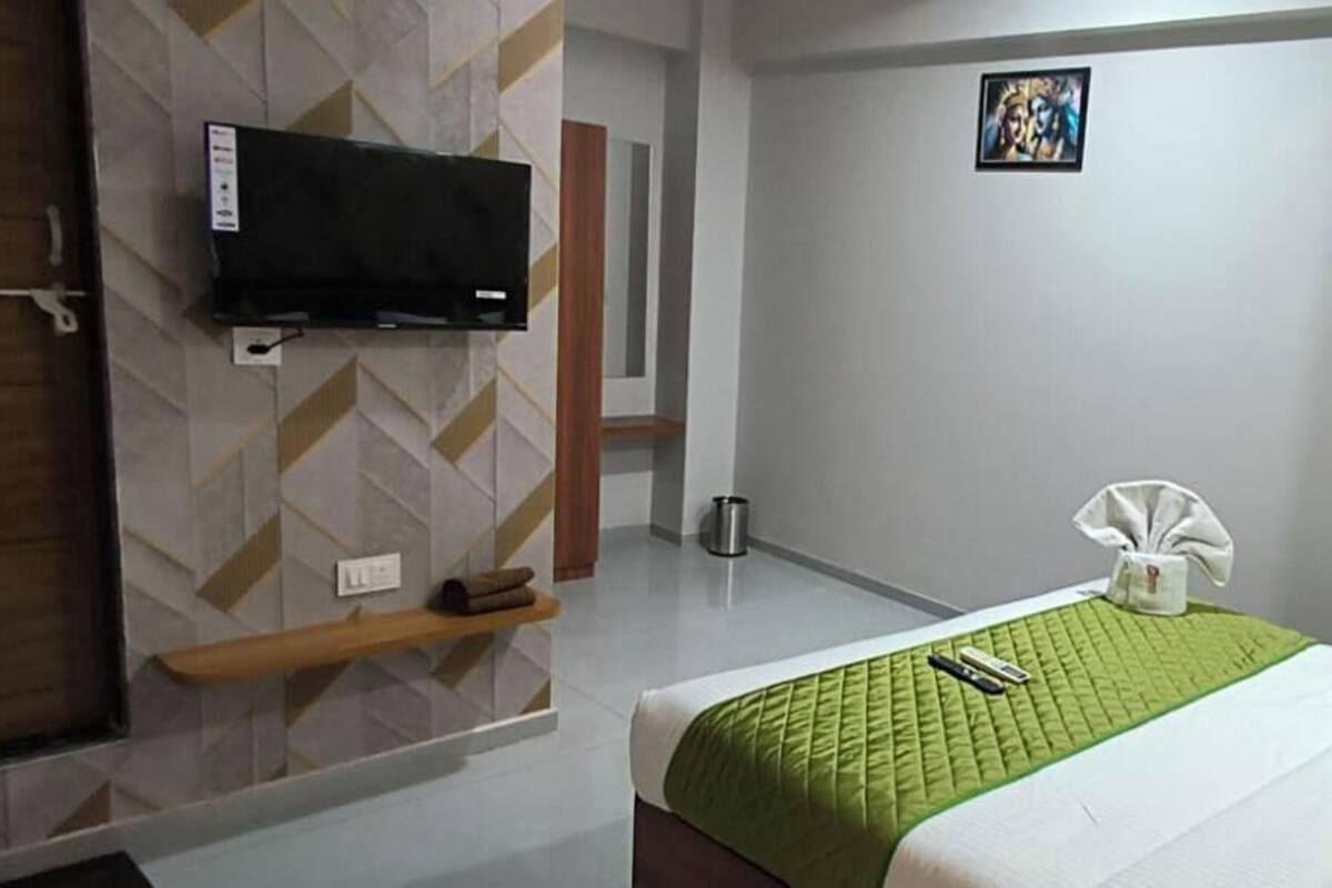 A hotel room with a bed, a TV mounted on the wall, a small shelf, and a picture on the wall.
