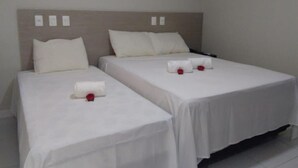Dos camas individuales con sábanas blancas, cabeceros de madera y una pequeña rosa roja sobre cada una.