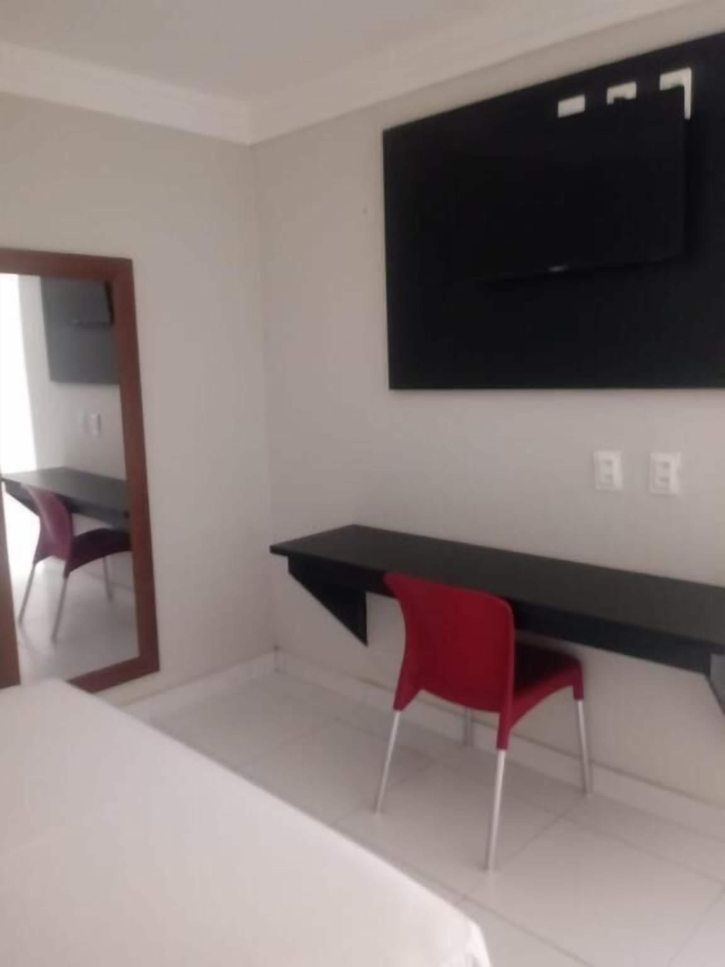 Una habitación de hotel con cama, escritorio con silla, televisión montada en la pared y espejo.