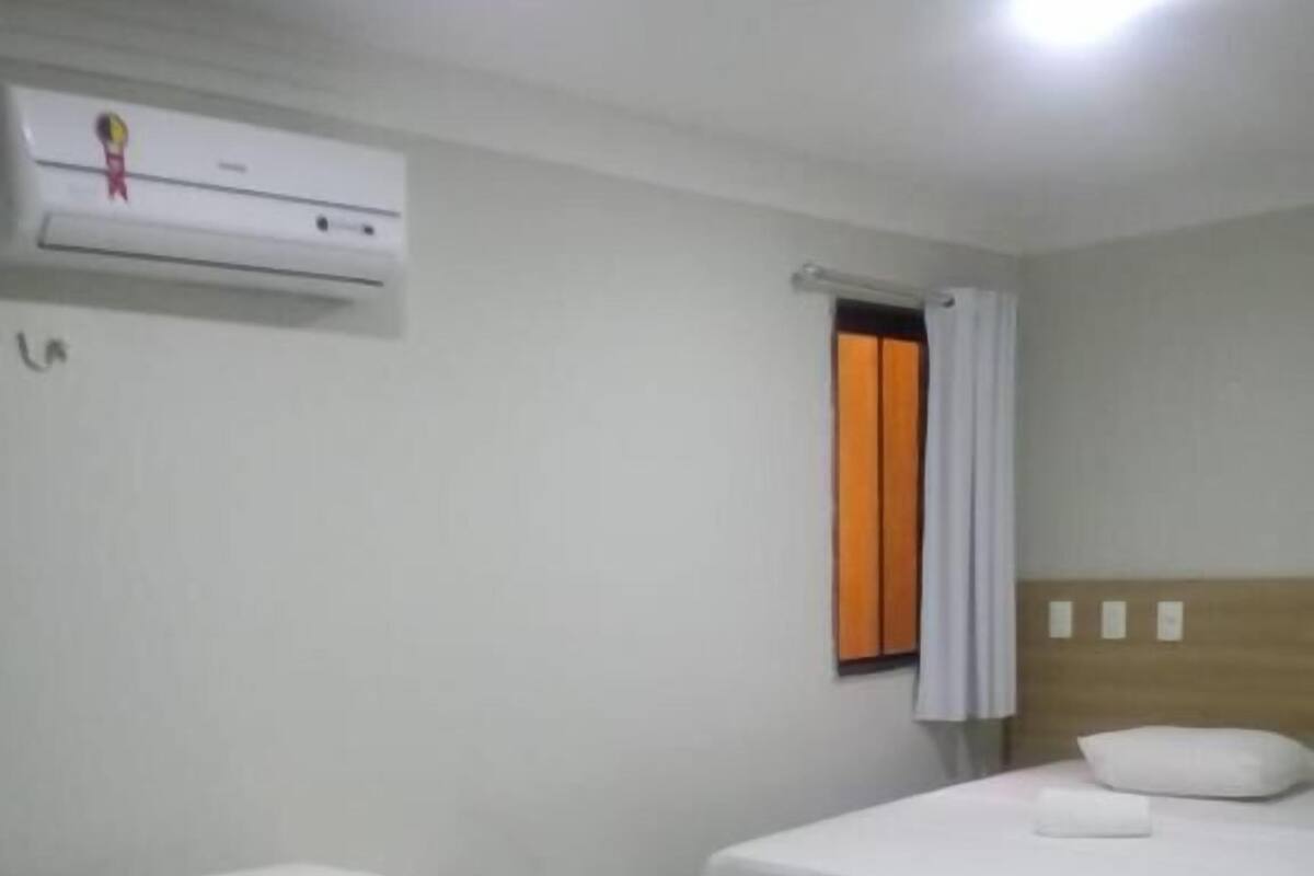 A hotel room with two single beds, a wooden headboard, an air conditioning unit, and a window with curtains.