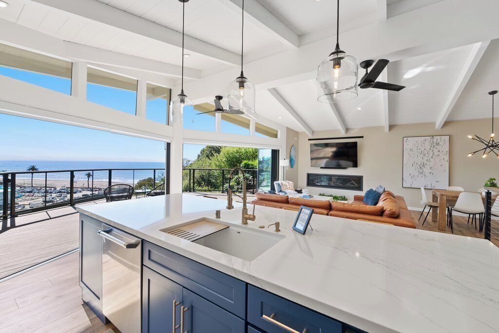 A modern kitchen with a large island, a dining area, and a balcony with a view of the ocean.