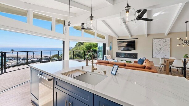 A modern kitchen with a large island, a dining area, and a balcony with a view of the ocean. - Seacliff Ocean View Escape (Aptos)