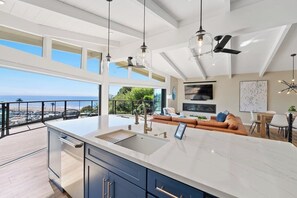 A modern kitchen with a large island, a dining area, and a balcony with a view of the ocean. - Seacliff Ocean View Escape (Aptos)