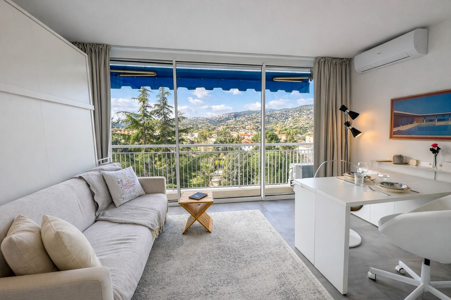 A modern hotel room with a balcony, a sofa, a desk, and a dining area.