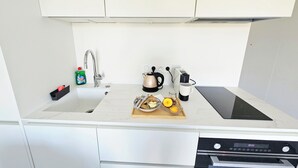 Moderni keittiö, jossa on pesuallas, vedenkeitin, kahvinkeitin ja leikkuulauta sekä ruoka-aineita.