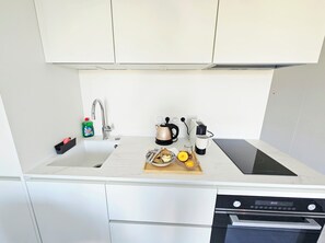 A modern kitchen with a sink, kettle, coffee maker, and a cutting board with food items. - Studio Marina Mandelieu - Stylish Studio on the French Riviera (Mandelieu-la-Napoule)