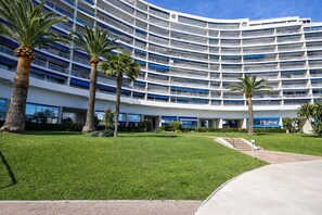 A multi-story hotel with a curved facade, palm trees, and a well-maintained lawn. - Studio Marina Mandelieu - Stylish Studio on the French Riviera (Mandelieu-la-Napoule)