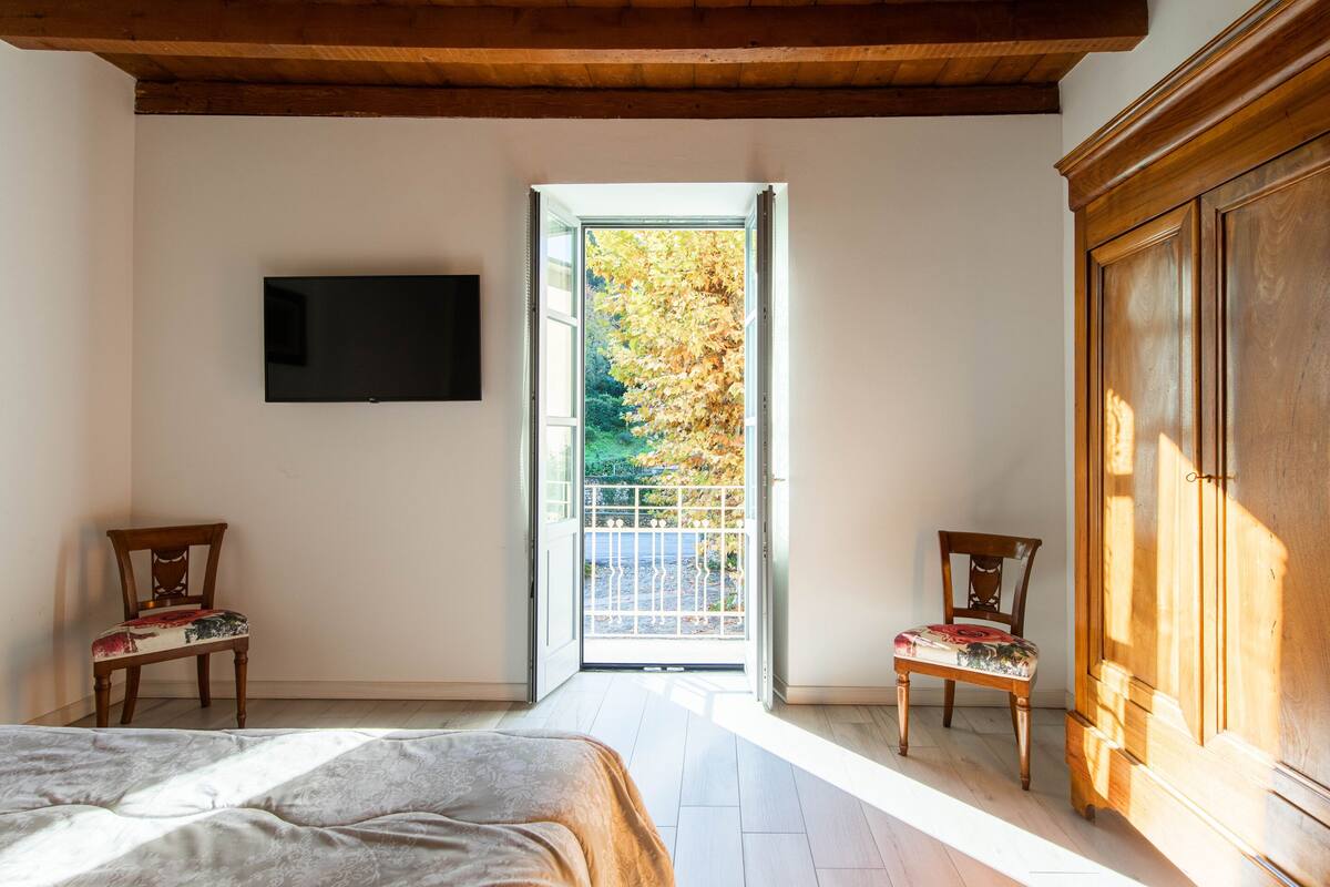 A bedroom with a bed, two chairs, a TV, and a large wooden wardrobe.