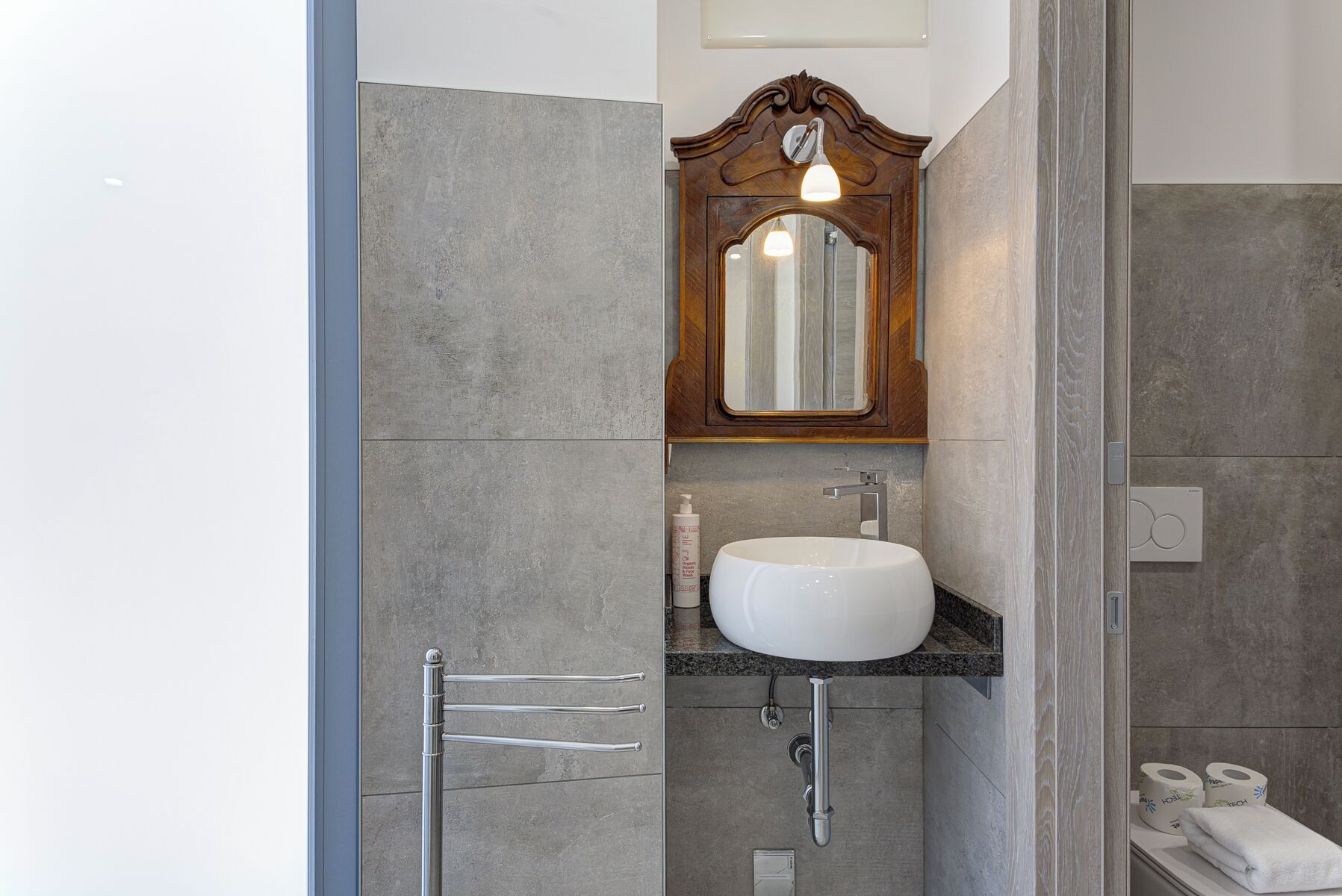 Une salle de bain avec un lavabo blanc, un miroir de coiffeuse en bois et un porte-serviettes.