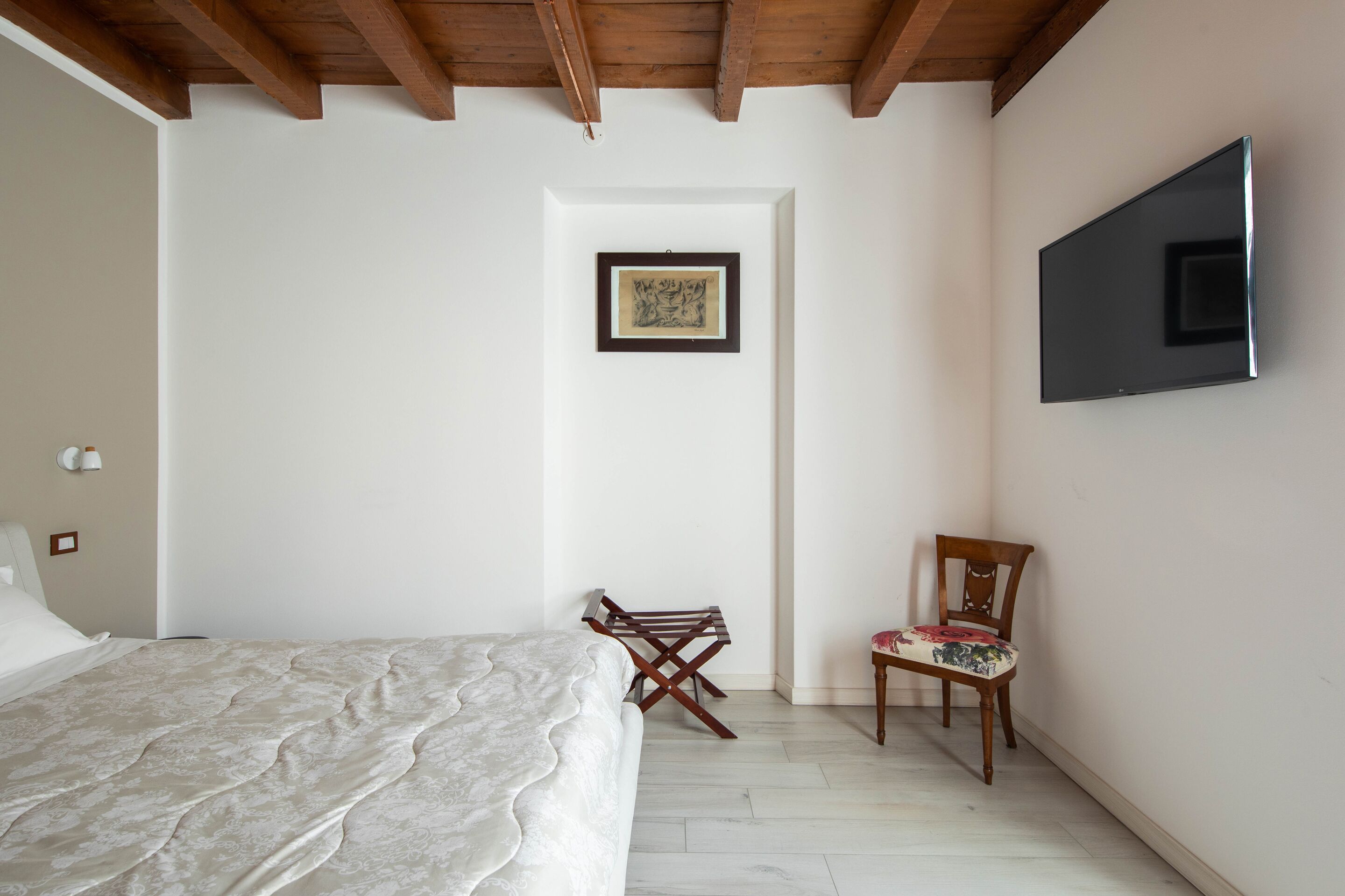 Un dormitorio con una cama, una silla, un televisor y un cuadro en la pared.
