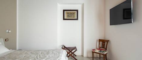 Un dormitorio con una cama, una silla, un televisor y un cuadro en la pared.