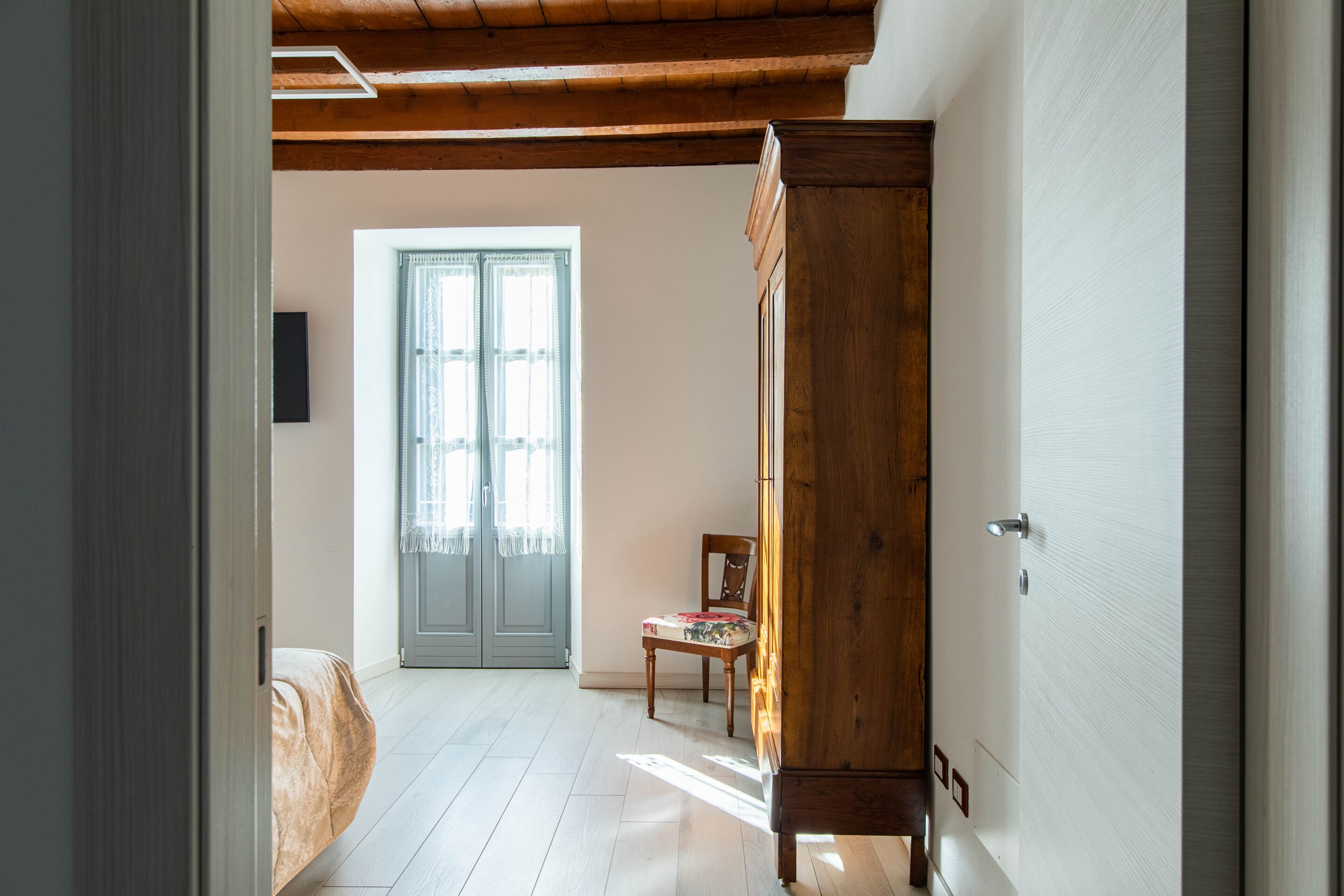 Um quarto com um armário de madeira, uma cadeira, uma cama e uma porta que dá para outro cômodo.