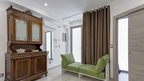 Ein Zimmer mit einem Holzkasten, einem grünen Sofa, einem großen Fenster und einer Tür.