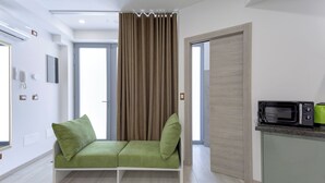 Ein modernes Zimmer mit einem grünen Sofa, einer Mikrowelle und einer Tür zu einem weiteren Raum.