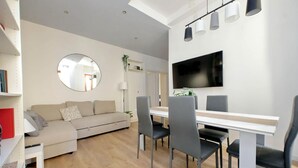 Ett modernt vardagsrum med en soffa, ett matbord, stolar, en tv och en spegel.