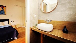 Ett hotellrum med en säng, ett sängbord, en spegel, ett badrum med handfat och en vägg av marmor.
