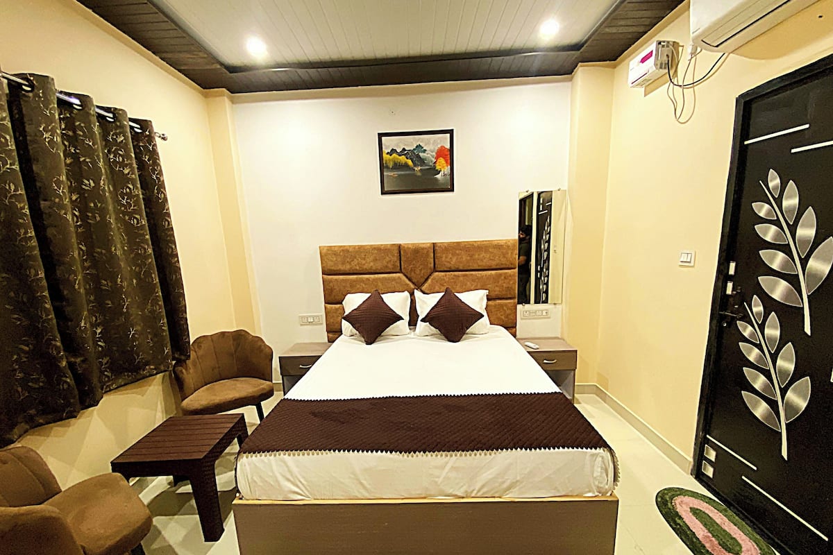Habitación de hotel con cama, una silla, una mesita, un cuadro en la pared y una puerta con diseño decorativo.