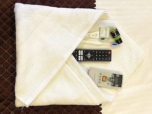 A bed with a white towel, a remote control, a bottle of shampoo, and a bottle of lotion.