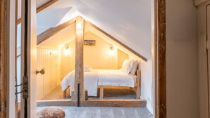 A bedroom with a sloped ceiling, a bed, a wooden bench, and a door. - Cliff Lane House, Cromer, Norfolk (Cromer)