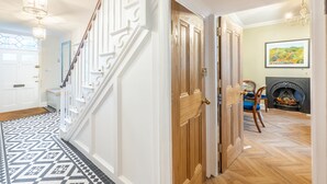 A hallway with a patterned floor, a staircase, a wooden door, and a fireplace with a painting above it. - Cliff Lane House, Cromer, Norfolk (Cromer)