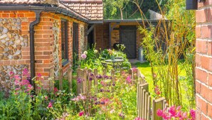 A rustic garden with a stone wall, wooden fence, and a metal table. - Old Church Hall, Glandford, Norfolk (Glandford)