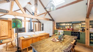 A rustic kitchen with wooden beams, a large wooden table, and a dining area with benches. - Old Church Hall, Glandford, Norfolk (Glandford)