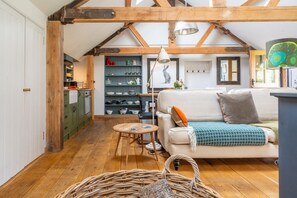 A cozy living room with a sofa, a small round table, a wicker basket, and a bookshelf with various items. - Old Church Hall, Glandford, Norfolk (Glandford)