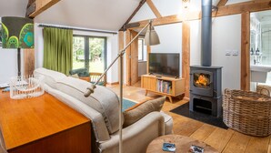 A cozy living room with a sofa, TV, fireplace, and a dining area with a table and chairs. - Old Church Hall, Glandford, Norfolk (Glandford)