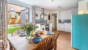 A kitchen with a dining table set for two, a washing machine, and a refrigerator. - Mollie's Cottage, Overstrand, Norfolk (Overstrand)