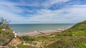 A coastal landscape with a beach, a wooden jetty, and a grassy hill. - Mollie's Cottage, Overstrand, Norfolk (Overstrand)