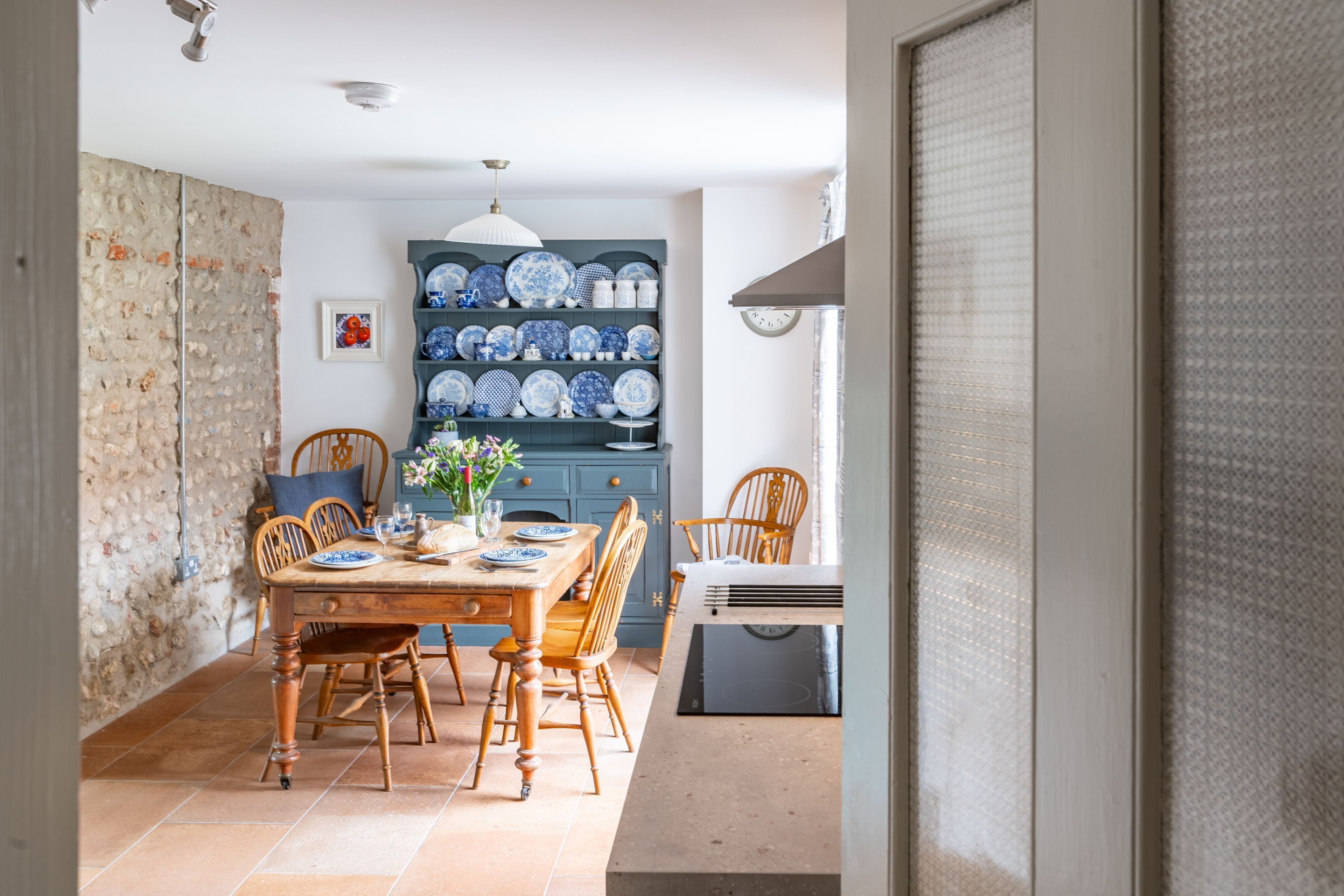 Un coin repas avec une table en bois, des chaises et un buffet bleu contenant de l’assiette.