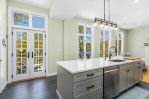A kitchen with a large island, double doors with glass panels, a sink, and a pendant light fixture. - Swan Dive - Waterfront Retreat in Cataumet RPLO032 (Bourne)
